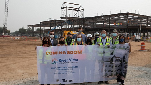 Construction workers hold Coming Soon sign for River Vista Behavioral Health hospital
