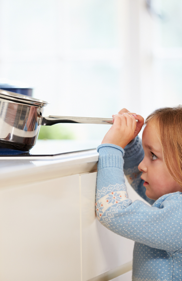 A little girl pulling down a pot from on top of a stove