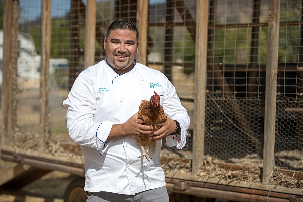 Chef Robert holding chicken and smiling at camera