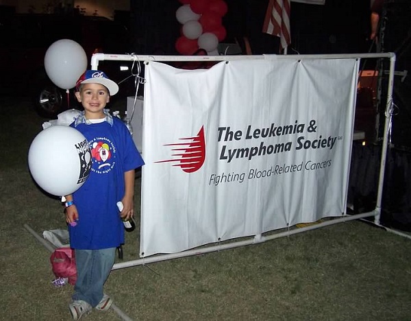 Photo of Jakob in front of a banner for The Leukemia and Lymphoma Society