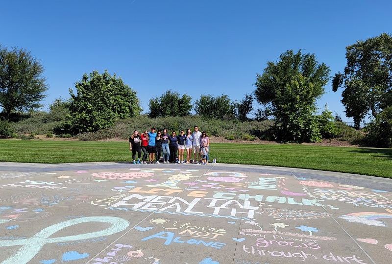 Foto de voluntarios de arte tiza «Let's Chalk About Mental Health» frente a la instalación artística
