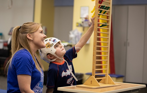Photo of rehabilitation therapist working with a young boy to reach clips on ladder