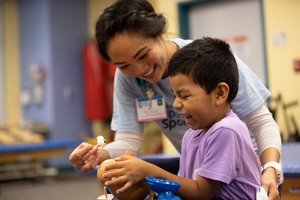 Foto de un terapeuta físico de <i>Valley Children's</i> sonriéndole a un niño