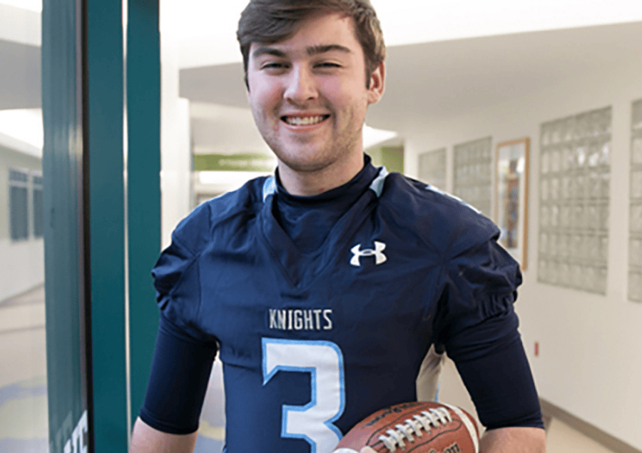 Un adolescente con una camiseta de fútbol sonríe mientras sostiene una pelota de fútbol