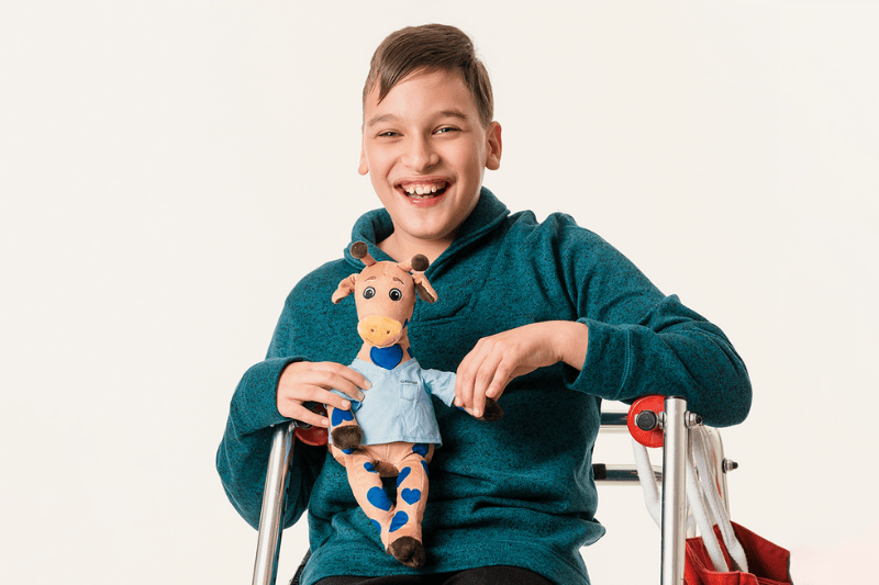 Un niño sonríe mientras sostiene un juguete de peluche de George la jirafa