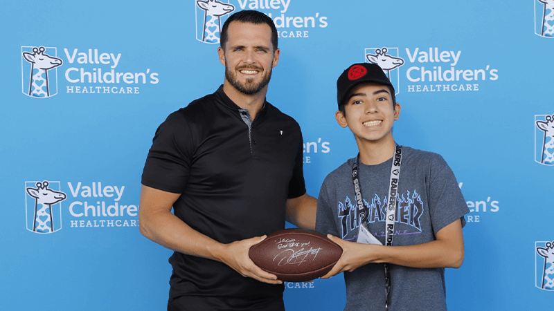 Derek Carr holds a signed football with a young boy