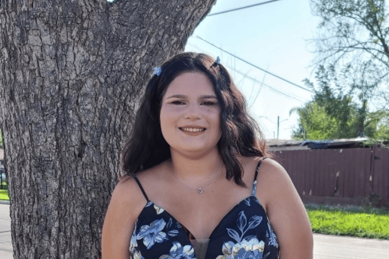 Una adolescente sonríe de pie junto a un árbol