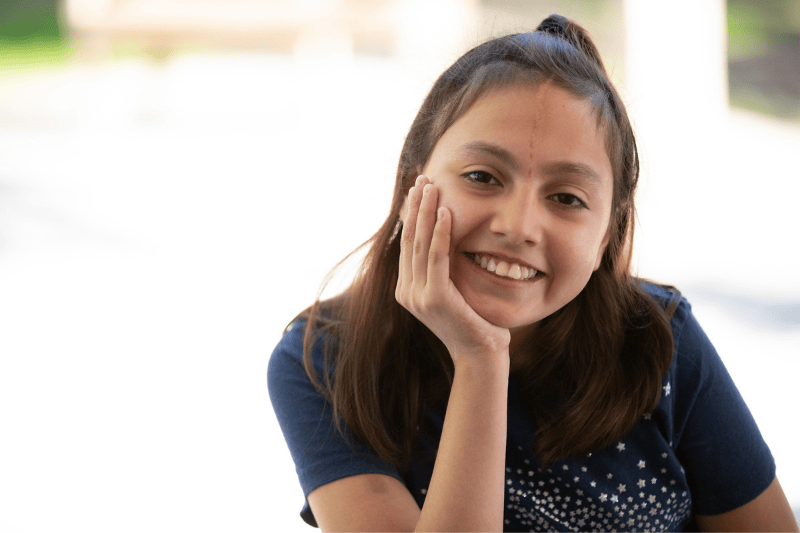 A teenage girl smiles, resting her chin upon her hand