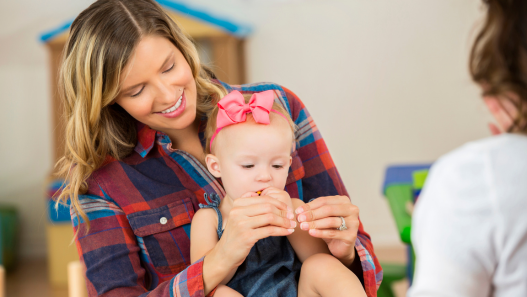 Mamá sosteniendo al bebé y enseñándole ASL (lengua de señas americano) para obtener más información