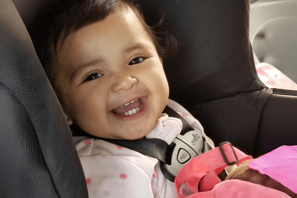 A baby smiles buckled securely in her car seat