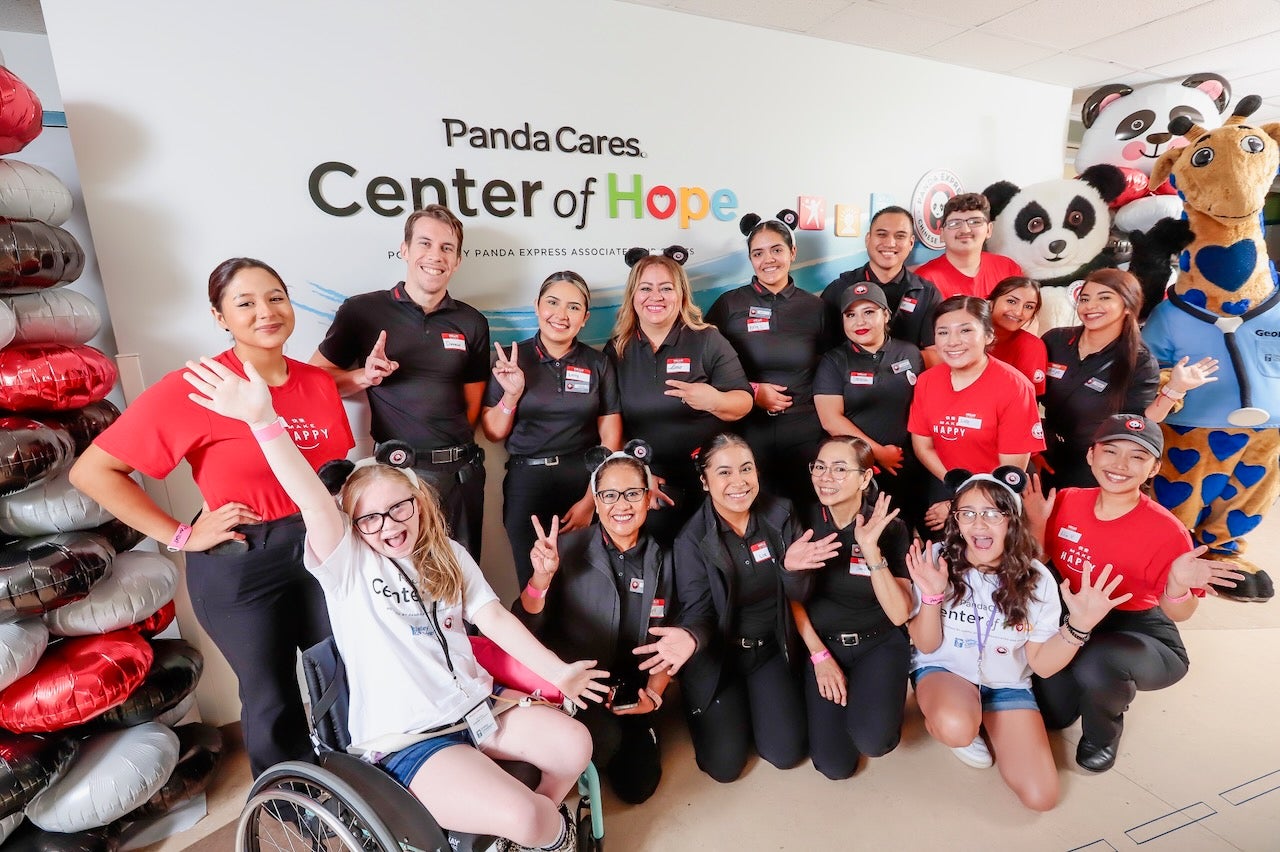 Panda Express employees and Norah, a CMN champion for Valley Children's pose in front of the Panda Cares sign