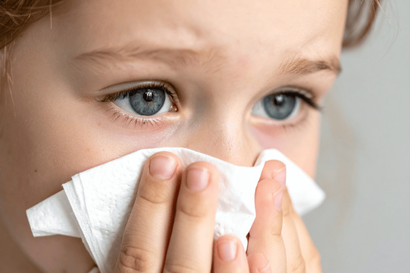 A young boy holds a tissue up to his face