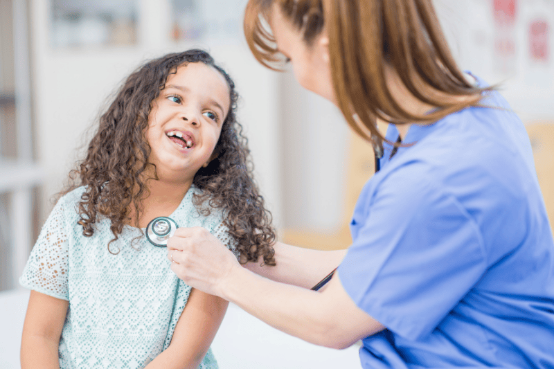 A nurse listens to a young girl's heartbeat as she smiles
