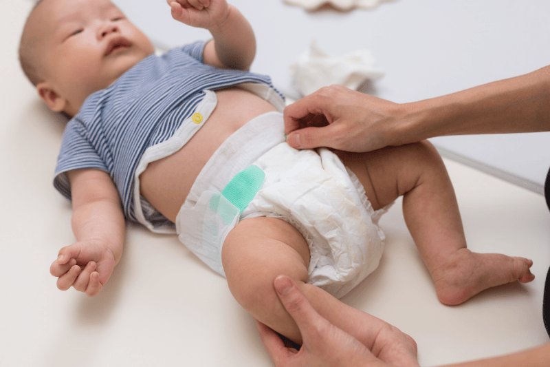 A baby lays on a mat while an adult finishes putting on their diaper