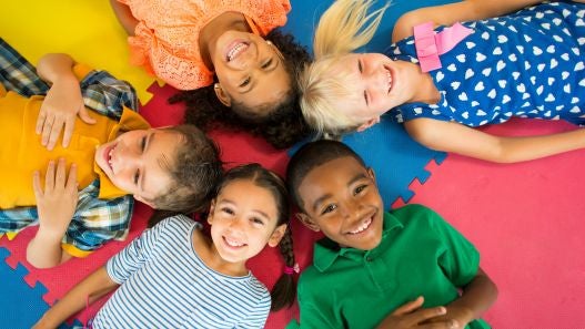 Children laying down in a circle smiling at camera