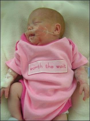 Kara in a onesie that says "worth the wait"