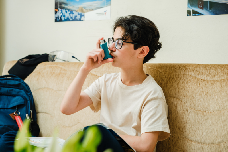 A boy uses an inhaler while seated on a couch.