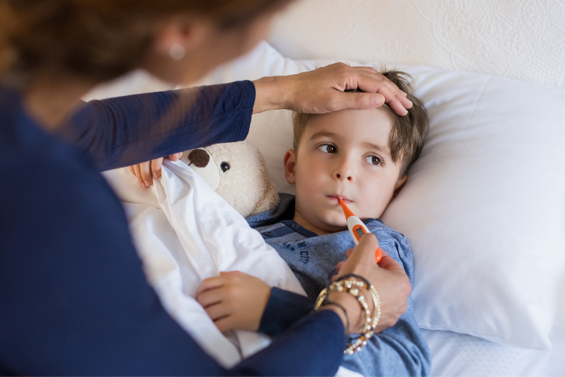 A boy lies in bed while an adult cares for him during a fever.