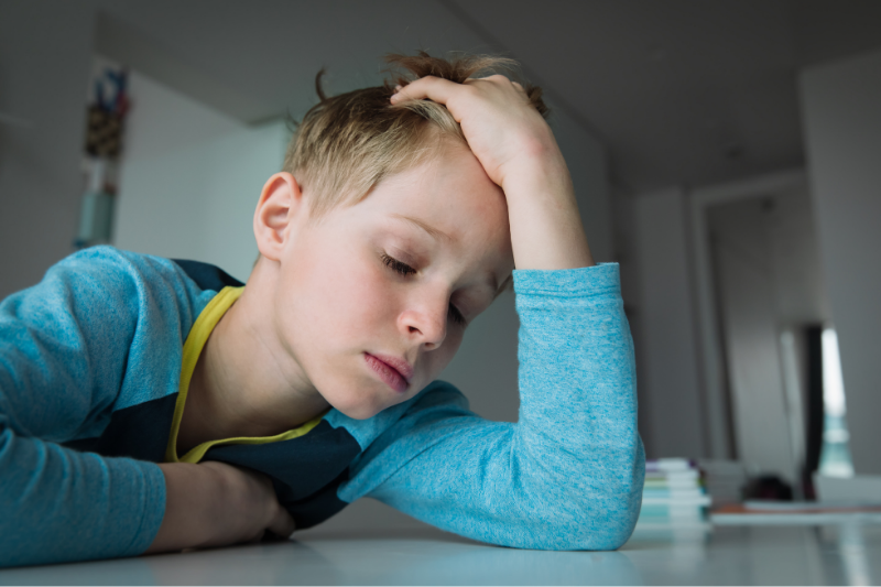 A boy leans over a table with his head in his hands.