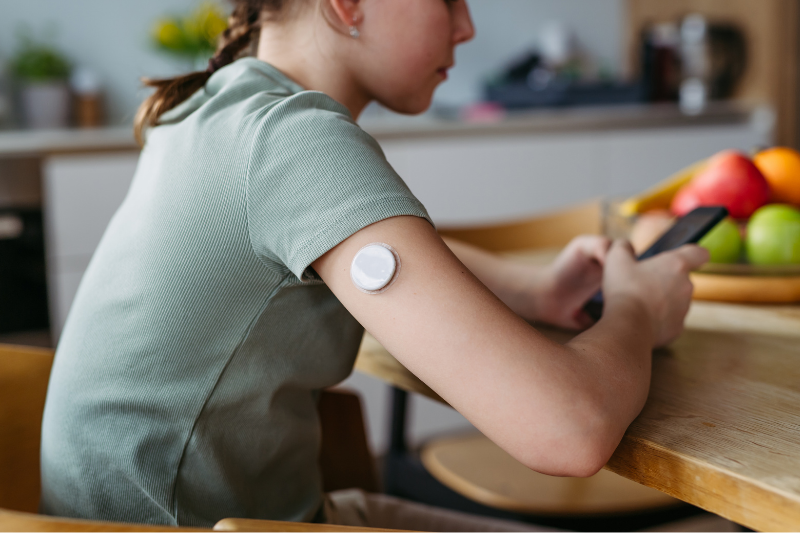 A girl sits at a table and wears a glucose monitor.