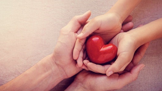 Child and adult holding hands with red heart