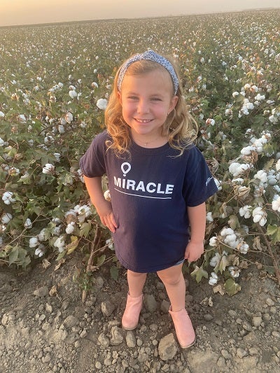 Foto de Joie de pie y sonriendo frente a un campo de algodón